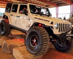 a white jeep is parked in a garage with rocks and boulders on the ground while people look at it