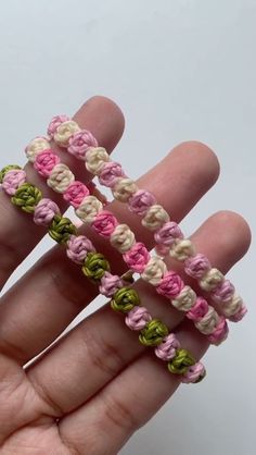 the hand is holding three small crocheted bracelets in pink, white and green