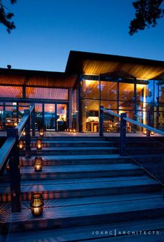 lit candles on the steps leading up to a large glass building at night with lights shining from windows