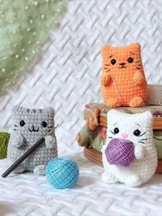 three crocheted cats sitting on top of a bed next to balls of yarn