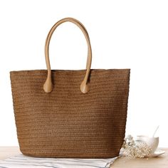 a brown straw bag sitting on top of a wooden table next to a white towel