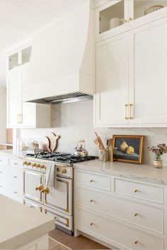 a kitchen with white cabinets and gold trim on the stove top, along with marble counter tops