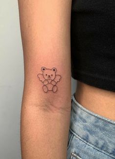 a small teddy bear tattoo on the left arm and right arm behind her is a woman's stomach