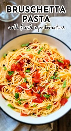 pasta with tomatoes and basil in a white bowl on top of a wooden table next to a glass of water