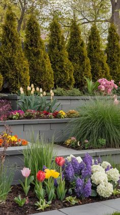 an assortment of colorful flowers and plants in a garden area with concrete steps leading up to trees