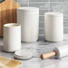 three white containers sitting on top of a counter next to a wooden cutting board and rolling pin