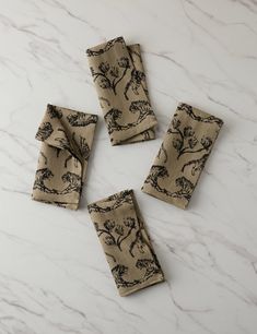 four napkins with trees printed on them sitting on a marble countertop next to each other