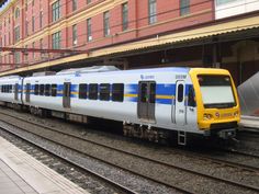 a yellow and blue train traveling down tracks next to a tall red brick building in the background