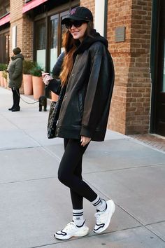 a woman in black jacket and leggings standing on sidewalk