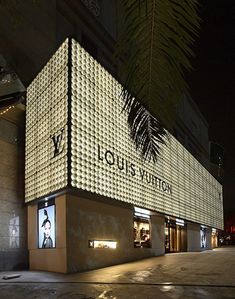 a building that is lit up at night with lights on the side and palm trees in front