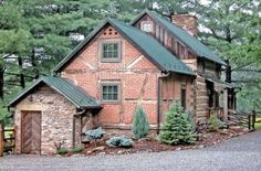 an old brick house with a green roof in the middle of some trees and gravel