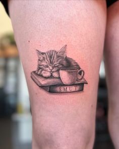 a cat laying on top of a book with a cup