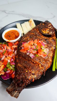 a black plate topped with meat and veggies on top of a white table