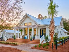 a white house with a blue roof and palm tree in the front yard at sunset