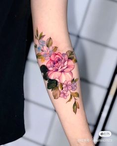 a woman's arm with pink flowers on it and green leaves around the wrist