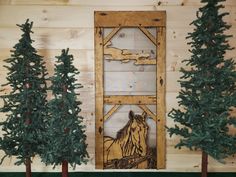 three small trees in front of a wooden door with a horse on it and another tree next to it