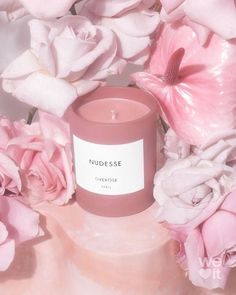 a candle surrounded by pink flowers on a white tablecloth with the words nudgesse printed on it