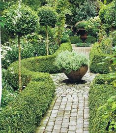 a stone path in the middle of a garden with trees and bushes on either side