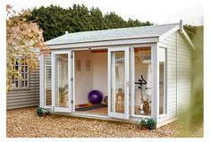 a small white shed sitting on top of a gravel field next to a building with doors open