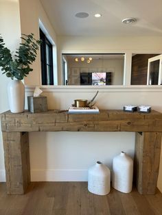 a wooden table with two vases and a mirror on the wall in front of it