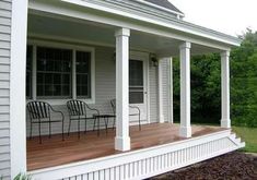 a porch with chairs on it next to a white house in the grass and trees