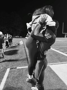 a woman is carrying a child in her arms on the football field while others watch