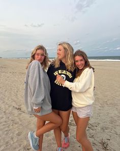 three girls are standing on the beach together