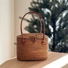 The Bali Athens Rattan Handbag is the perfect accessory for any stylish woman. This beautiful, handmade rattan bag is made by skilled artisans in Bali, using natural materials to create a one-of-a-kind piece that is both fashionable and functional. The Hailey design is sleek and versatile, making it the perfect bag for everyday use or a night out. With its spacious interior and beautiful design, the Bali Hailey Rattan Handbag is sure to impress. Shop now and add a touch of Bali to your wardrobe! Handheld Satchel With Braided Handles In Natural Color, Brown Palm Leaf Bag For Daily Use, Brown Rattan Tote Straw Bag, Top Handle Rattan Shoulder Bag For Vacation, Brown Palm Leaf Shoulder Bag For Daily Use, Brown Palm Leaf Shoulder Bag For Travel, Rattan Open Weave Straw Bag For Everyday Use, Rattan Straw Bag With Open Weave For Everyday Use, Rectangular Rattan Straw Bag With Open Weave