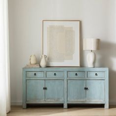 a blue dresser with two vases and a painting on the wall in front of it