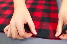 someone is sewing on a red and black checkered blanket with their hands over the edge