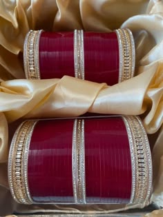 two red and gold bracelets sitting on top of a satin covered bag with ribbon