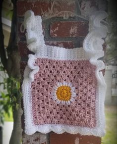 a pink and white crocheted square with a yellow flower on it hanging from a brick wall