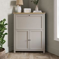 a white cabinet with two plants on top and a lamp in the corner next to it