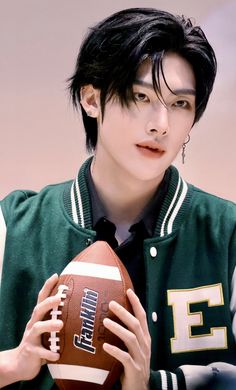 a young man holding a football in his hand and wearing a green jacket with the letter e on it