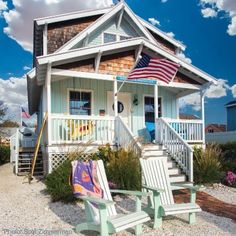 two lawn chairs sitting in front of a white house with an american flag on the porch