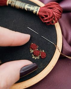 a woman's hand is holding a needle and thread in front of a embroidery hoop