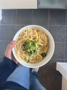 a person holding a bowl of noodles with broccoli