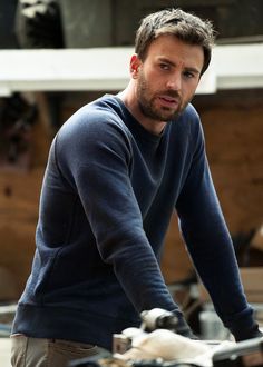 a man riding a bike in front of a wooden building with an airplane behind him