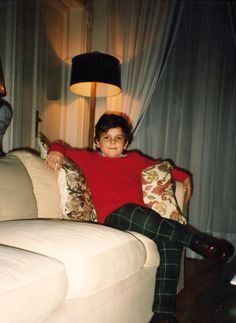 a young boy sitting on top of a white couch next to a lamp in a living room