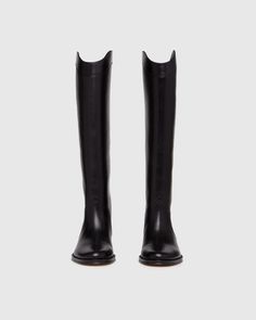 Raina is our take on the classic riding boot. Crafted from a super durable yet luxuriously soft black leather, this timeless straight shaft tall boot is designed with a curved topline that dips at the front and back for a flattering look, western-inspired pattern and stitch detailing, an extended leather welt with tonal stitch details, and a black leather stacked 20mm heel for a slight amount of lift. The classic menswear-inspired details on the outsole include stitching and half toplift for an Black Tall Boots Women, Womens Tall Black Boots, Tall Boots Outfit, Riding Boot Outfits, Tall Western Boot, Capsule Wardrobe Women, Classic Menswear, Womens Riding Boots, Fall Boots