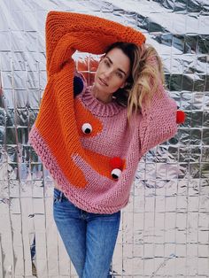 This woolly magical hug in orange and pink might be the perfect way to show off your wacky and whimsical personality. The bold and vibrant colours would make you stand out in a crowd and make you feel like you're floating on a cloud of happiness. The chunky knit of the sweater gives it a cosy, comfortable feel, making it the perfect choice for a happy person like you.  Featuring 5 removable pom-poms, this sweater lets you customize your look and switch up your style in an instant. The pom-poms a Playful Crew Neck Knitted Sweater, Playful Pink Crew Neck Sweater, Playful Knitted Winter Sweater, Oversized Pink Knitted Sweater, Pink Acrylic Winter Sweater, Cute Chunky Knit Sweater For Fall, Orange Chunky Knit Sweater For Fall, Cute Multicolor Winter Sweater, Pink Chunky Knit Acrylic Sweater