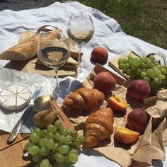 an assortment of food and wine on a picnic blanket with bread, grapes, peaches, and croissants