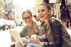 two young women sitting on the sidewalk using a tablet