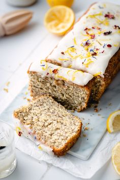 a loaf of lemon cake with icing and sprinkles next to sliced lemons