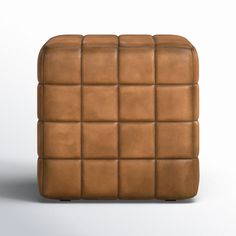 a brown leather ottoman with square squares on the top and bottom, sitting in front of a white background