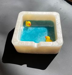 two yellow rubber ducks in a blue water filled bathtub on a gray table top