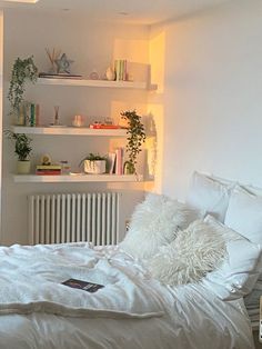 a bed with white sheets and pillows in a room next to a wall mounted bookshelf