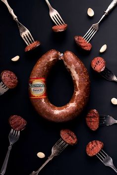 a large sausage and some forks on a table with other food items around it,