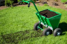 a green wheelbarrow filled with dirt in the grass