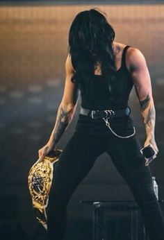 a man with long black hair and tattoos holding a gold belted glove on stage